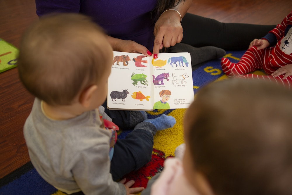 Teacher points to animal in book as baby looks on