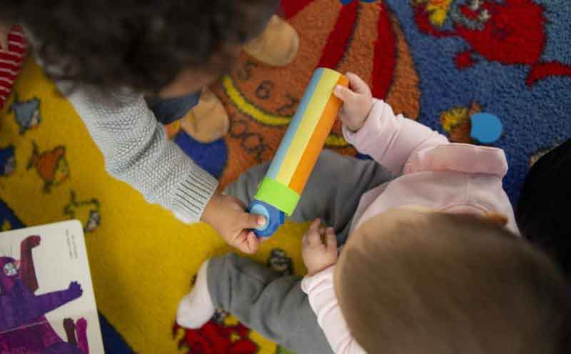 Baby and toddler both hold onto same colorful toy
