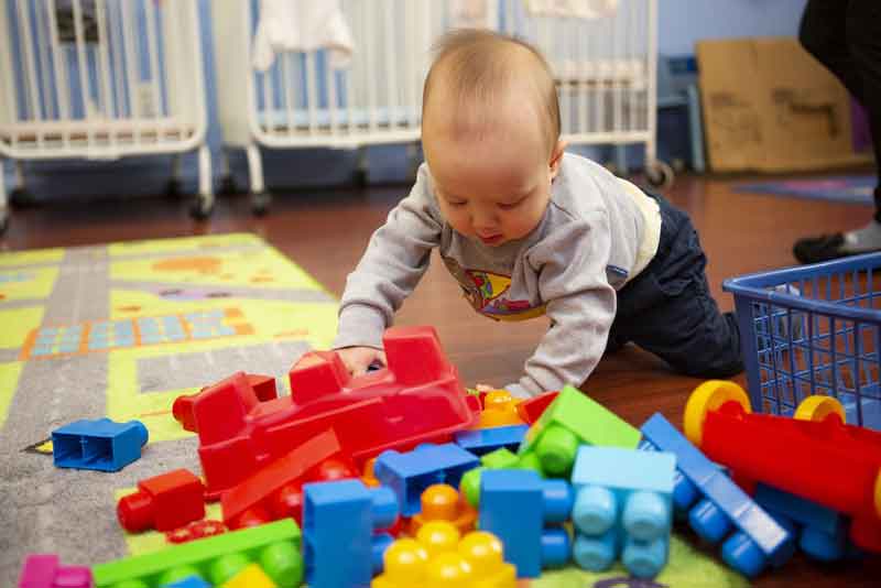 Baby looking at pile of big building blocks in classroom