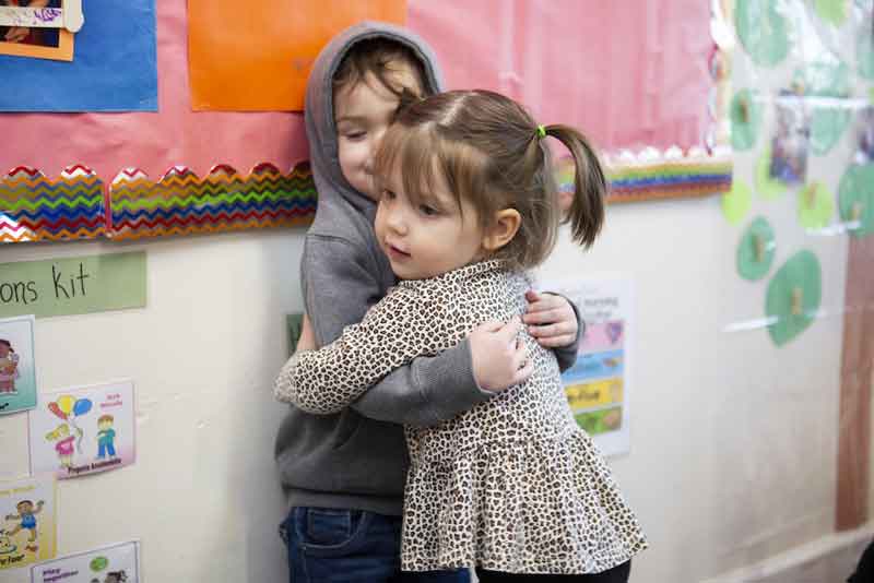 Two toddlers hug in a classroom