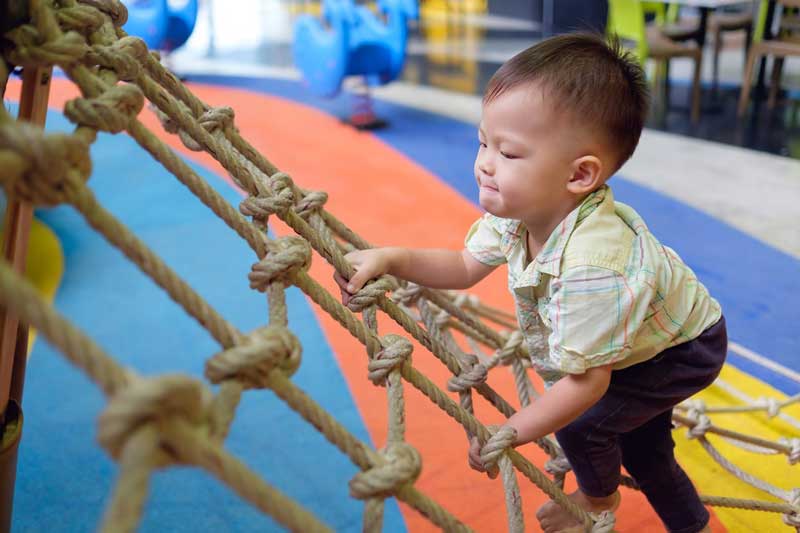 Toddler boy having fun trying to climb on jungle gym
