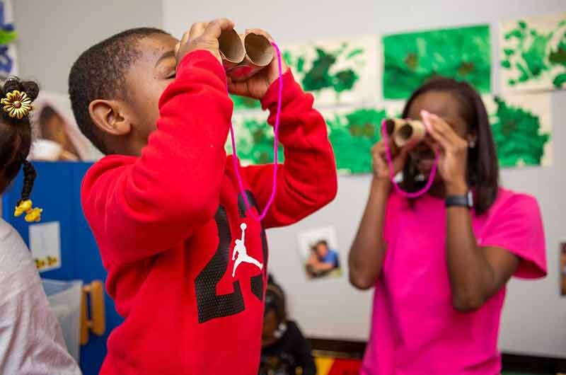 Young boy and teacher pretending to use fake binoculars