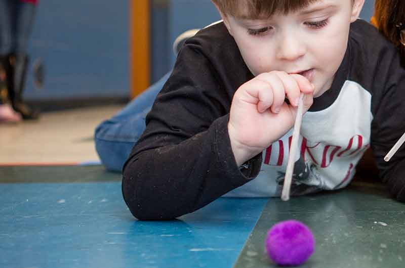 Young boy blowing cotton ball with a straw