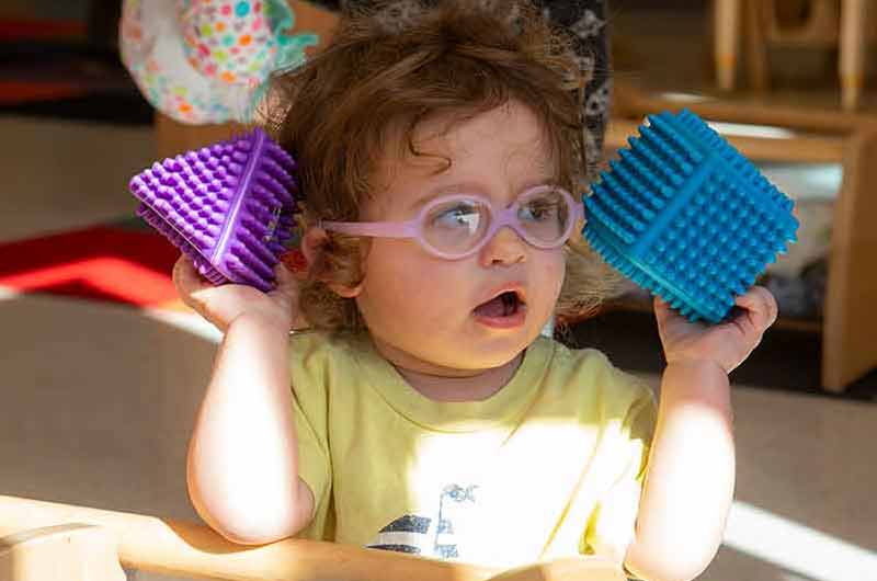 An older infant holding a pyramid and cube building block