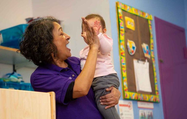 Educator holds an infant, and they exchange a high-five