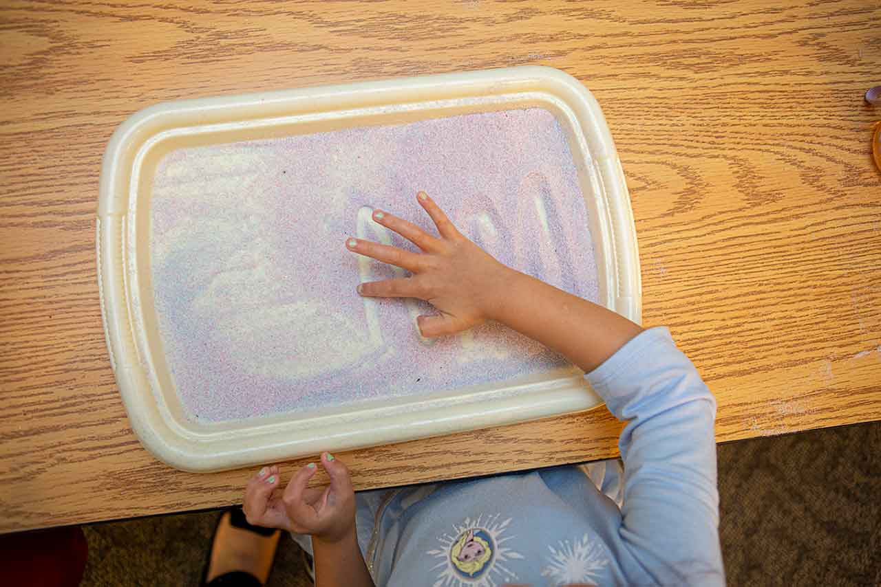 Child making letter shapes in tray with sand