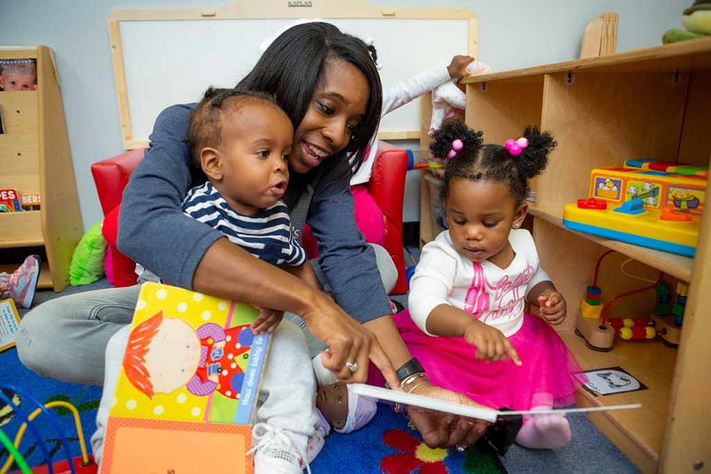 Teacher points at book while sitting on floor with two toddlers