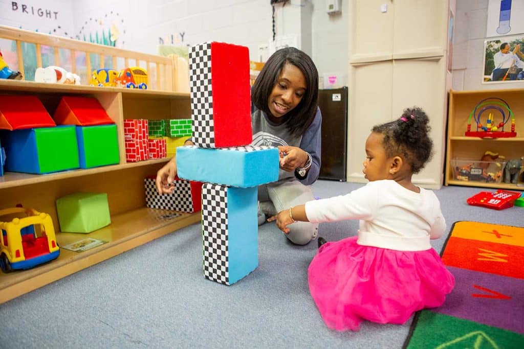 An educator and a toddler point to stacked blocks