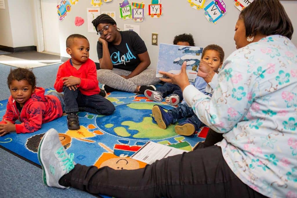 Children on floor listening as teacher holds a book