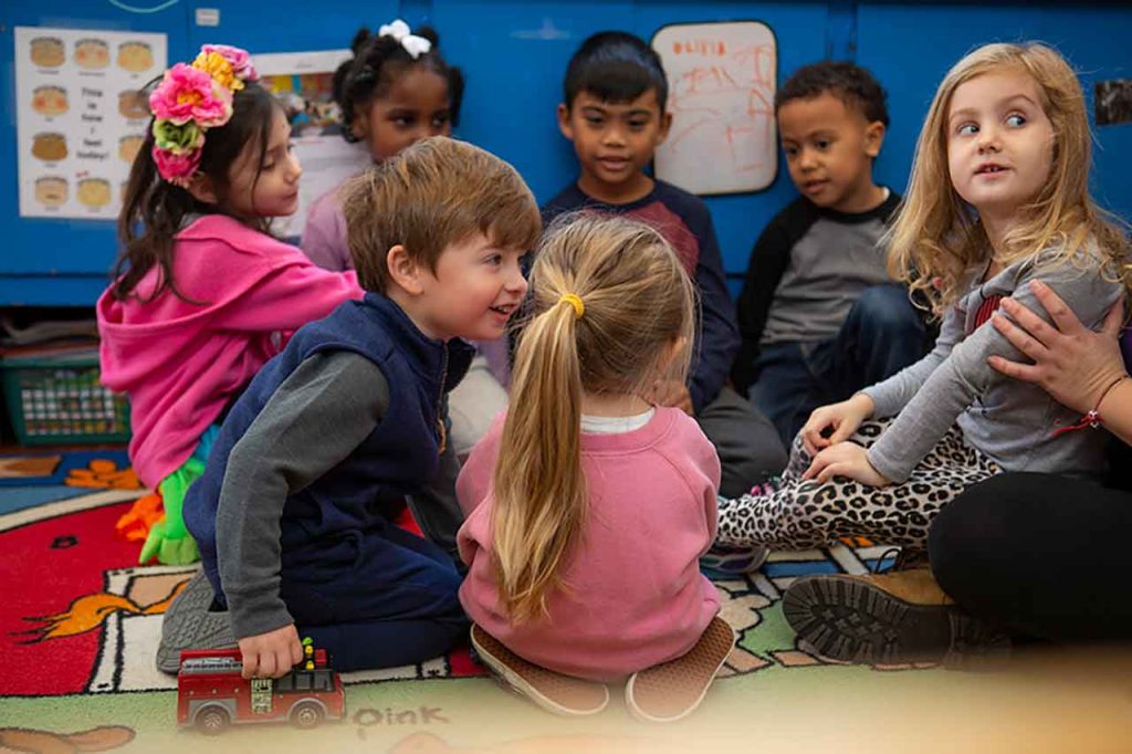 Children sitting in circle on floor with one child talking to another child