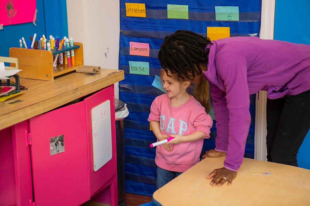 Child and educator look at white board with writing together